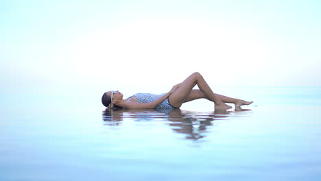 Woman-in-Swimsuit-Lying-on-Infinity-Pool-Border-Merging-With-Sea-Horizon-and-Sky