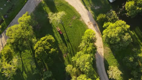Aerial-top-down-of-Red-tractor-cutting-green-grass-in-Park-during-sunset-time--Uruguay,South-America