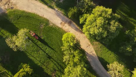 Aerial-view-of-a-red-tractor-trailer-cutting-grass-in-the-park-Uruguay,-top-down-view