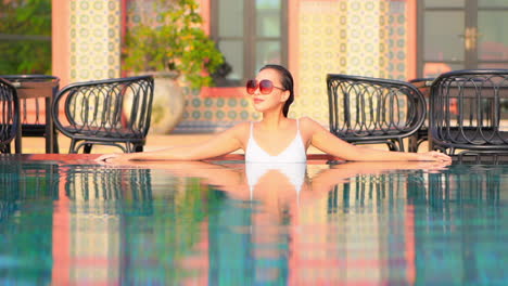 A-young-woman-leans-back-along-the-water-edge-of-a-resort-pool