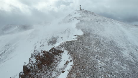 Pico-De-Montaña-Con-Torre-De-Telecomunicaciones-En-Condiciones-De-Frío-Invierno,-Viento-Y-Nieve,-Vista-Aérea-De-Drones