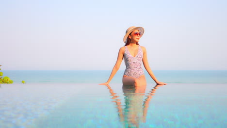 A-young-fit-woman-in-a-pretty-printed-one-piece-swimming-suit-sits-on-the-edge-of-an-infinity-edged-pool