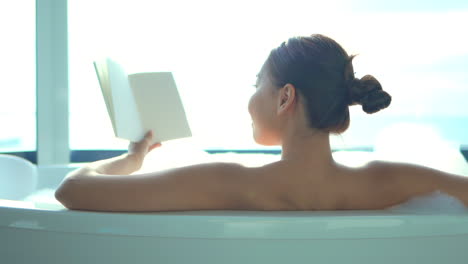Back-to-the-camera,-a-sexy-young-woman-in-a-luxurious-bubble-bath-contemplates-the-blank-page