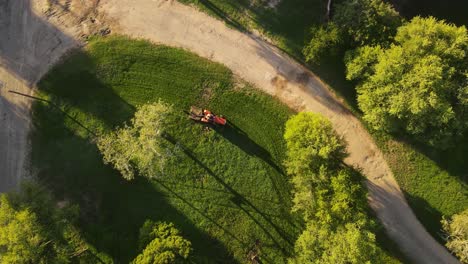 Aerial-directly-above-red-tractor-cutting-green-grass,-Fray-Bentos-park-in-Uruguay