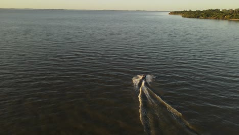Slow-motion-aerial-view-behind-jetski-on-lake-during-sunset