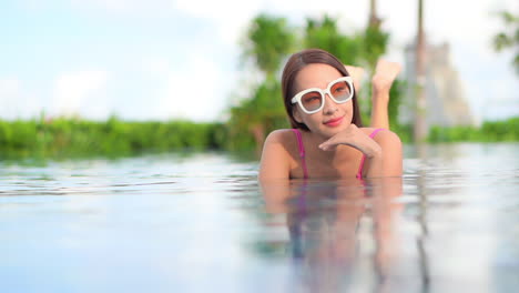 A-pretty-young-woman-lying-on-her-stomach-in-a-resort-swimming-pool-smiles-as-she-looks-around-at-the-scenery