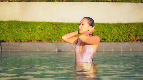 Slim-asian-woman-in-swimsuit-fixing-her-wet-hair-after-swim-in-swimming-pool-of-luxury-resort