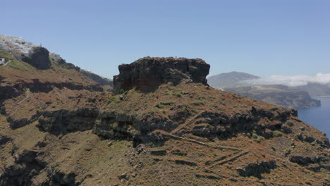 Antenne:-Panorama-Überflugaufnahme-Eines-Mannes,-Der-Auf-Dem-Skaros-Felsen-In-Santorini,-Griechenland,-Spazieren-Geht