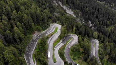 Aerial-view-of-the-turns-of-Maloja-Pass-in-Engadin,-Switzerland-with-cars-and-a-yellow-bus-driving-up-and-down-on-the-road
