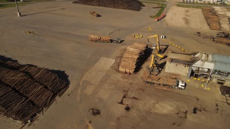 Drone-shot-of-industrial-cranes-grabbing-trunks-of-loaded-trucks-in-paper-mill-factory