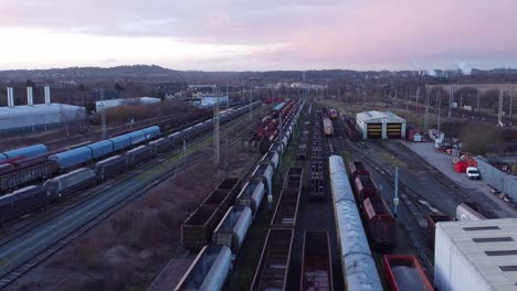 Sunrise-aerial-view-of-long-railroad-tracks-with-heavy-diesel-locomotive-carriages-and-cargo-container-yard-low-slow-forward-shot