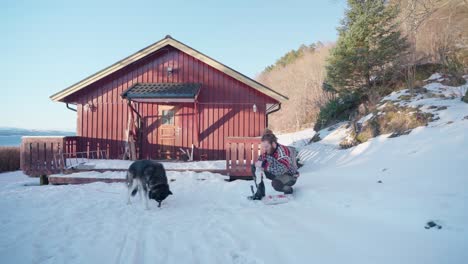 Mann-Füttert-Seinen-Alaskischen-Malamute-Hund-Im-Winter-Vor-Der-Holzhütte