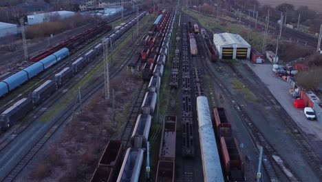 Sunrise-aerial-view-of-long-railroad-tracks-with-heavy-diesel-locomotive-carriages-and-cargo-container-yard-tilt-up-reverse-shot