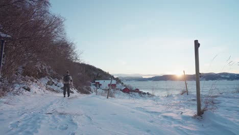 Hombre-Con-Mochila-Caminando-Por-Un-Camino-Nevado-Al-Atardecer-En-Vikan,-Indre-Fosen,-Noruega