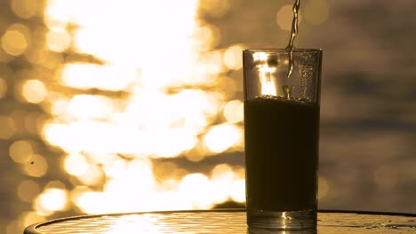 Amber-Ale-Lagerbier-Wird-In-Ein-Glas-Mit-Dem-Meer-Und-Dem-Sonnenuntergang-Im-Hintergrund-Gegossen