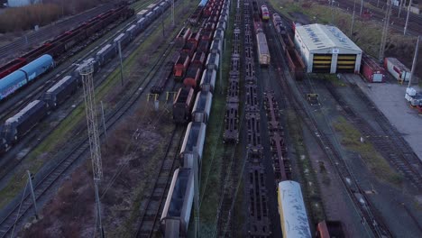 Sunrise-Luftbild-Von-Langen-Eisenbahnschienen-Mit-Schweren-Diesellokomotivwagen-Und-Frachtcontainer-Hof-Aufsteigender-Vogelperspektive