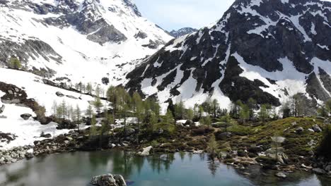 Vista-Aérea-Del-Lago-Mässersee-En-El-Remoto-Valle-De-Binntal-En-Valais,-Suiza-A-Principios-De-Verano-Mientras-Las-Montañas-Circundantes-Todavía-Están-Cubiertas-De-Nieve