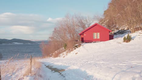 Red-Wooden-Cottage-By-The-Lakeshore-On-Snow-Mountains-Near-Vikan-In-Indre-Fosen,-Norway
