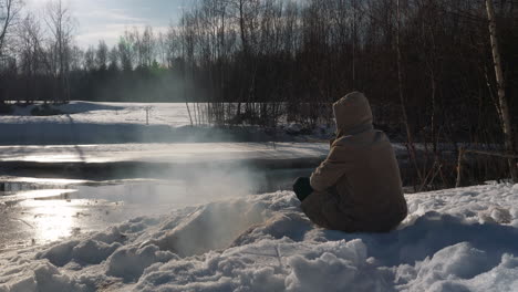 Portrait-of-man-by-frozen-river-stream,-surviving-in-wild-winter-nature