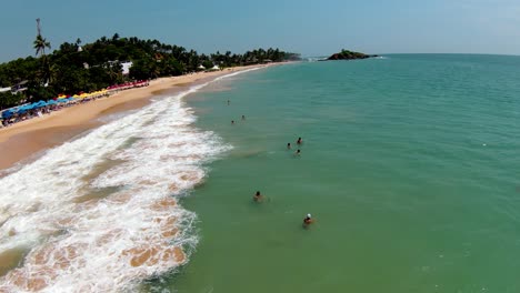 Aerial-dolly-in-flying-over-people-swimming-in-turquoise-sea-near-sand-shore-in-Mirissa-beach-at-daytime,-Sri-Lanka