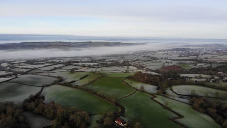 Aerial-rising-shot-over-frozen-Devon-farmland-on-a-frosty-morning-with-river-mist-in-the-background