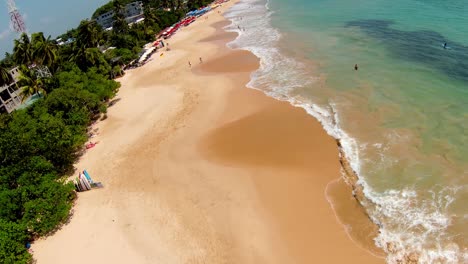 Aerial-Drone-Over-Popular-Tourist-Beachfront-Destination-In-Sri-Lanka-Panning-Over-People-On-Sand-On-Sunny-Day
