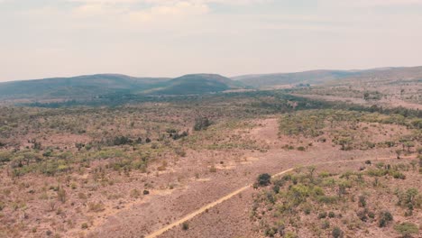 Dirt-road-in-african-savannah-bush-with-trees-and-hills,-drone-shot