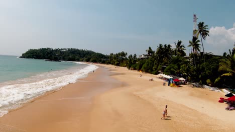 Aerial-Drone-Over-Popular-Sandy-Tourist-Beach-In-Sri-Lanka-On-Sunny-Day-With-Blue-Skies-And-Tropical-Palm-Trees