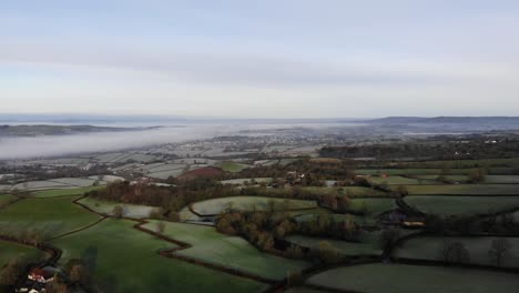 Aerial-panning-right-shot-of-the-Otter-Valley-countryside-in-East-Devon-England-on-a-sunny-morning-with-low-lying-river-mist-in-the-distance