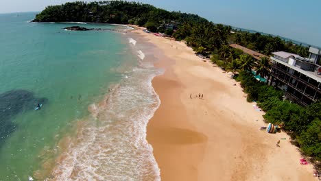 Aerial-Footage-Of-Wide-sandy-Beach-With-Large-Arriving-And-breaking-ocean-Waves-In-Bay-Of-Beautiful-Sri-Island,-Sri-Lanka