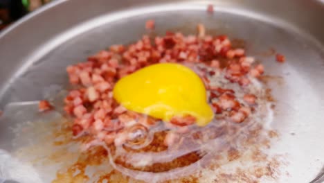 Close-up-of-hand-cracking-egg-in-a-camping-pan-with-bacon