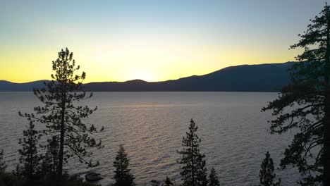 Blick-Auf-Den-Sonnenuntergang-Auf-Dem-Bergsee-Durch-Pinien-Am-Ufer-Des-Lake-Tahoe-In-Den-Bergen-Der-Sierra-Nevada---Luftdrohne-Fliegt-Durch