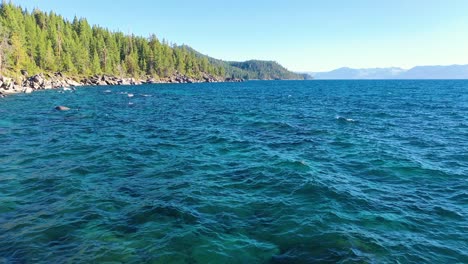 Flying-Over-Wind-And-Waves-at-Lake-Tahoe-Searching-Over-Clear-Blue-Turquoise-Water-And-Rocky-Shoreline-with-Pine-Tree-Forest---aerial-drone-shot