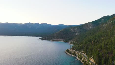 Coches-Conduciendo-Por-Una-Hermosa-Carretera-Junto-Al-Lago-Con-Montañas-Y-Agua-Azul-Del-Lago-Tahoe-En-La-Sierra-Nevada-En-Un-Día-Nublado
