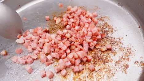 Close-up-zooming-into-camping-pan-with-bacon-cubes-stirred-with-a-metal-spoon