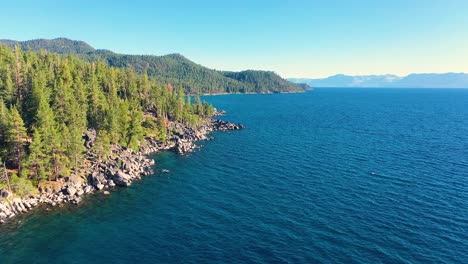 Aerial-Drone-Flying-Over-Clear-Blue-Waters-of-Lake-George,-New-York-With-Rocky-Shoreline-And-Thick-Pine-Tree-Forest-In-Mountains