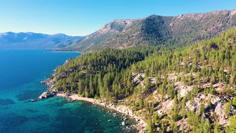 Kalifornische-Berge-Am-Lake-Taho-Mit-Kristallklarem,-Türkisblauem-Wasser-Und-Strand-Mit-Steinsteg-Und-üppigem-Kiefernwald---Luftdrohnenaufnahme