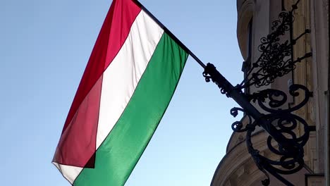 Red,-white-and-green-stripes-of-the-Hungarian-flag-flutter-quietly-from-a-gustatory-pole-on-a-Budapest-facade-on-a-sunny-day-in-the-wind