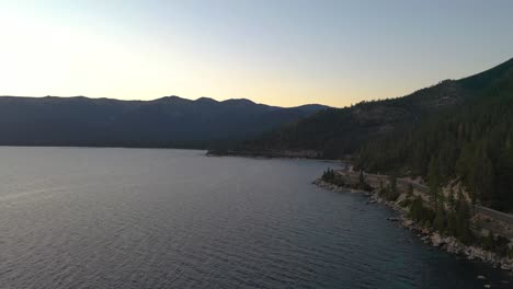 Beautiful-Alpenglow-in-Mountains-of-Lake-Taho-Over-Pristine-Calm-Waters-and-Pine-Tree-Forest-In-California-at-Sunset---aerial-drone-shot-panning-left