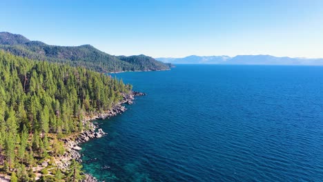 Lake-George,-New-York-Crystal-Clear-Blue-Waters-And-Lush-Pine-Tree-Forest-And-With-Mountains-and-Rocky-Shoreline---aerial-drone-reveal