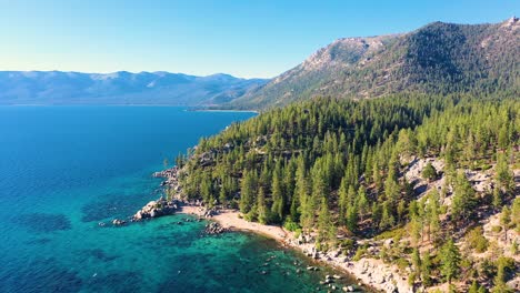 Aerial-Drone-View-of-Lale-Taho-Mountains-And-Thick-Pine-Tree-Forest-In-The-Sierra-Nevada-with-Crystal-Clear-Blue-Water-And-Beach-With-Boulders-And-Rock-Jetty