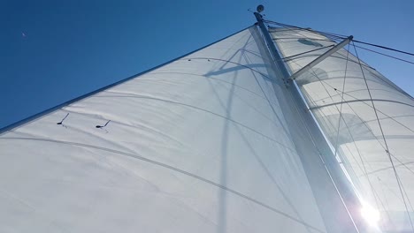 Vertical-view-of-catamaran-mast-and-white-sail-at-sunny-weather-and-blue-sky