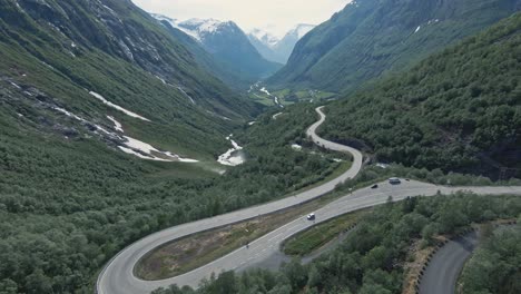 Winding-mountain-valley-road-with-driving-vehicles-in-Stryn,-Norway,-aerial-FPV-view