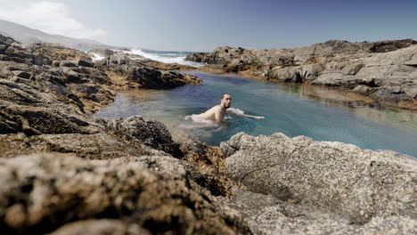 Young-caucasian-male-in-swimwear-bathing-inside-natural-ocean-pool-formation-in-Fuerteventura-canary-island-Spain