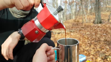 Close-up-of-a-man-pouring-coffee-in-a-mug-in-a-camping-place-in-the-forest