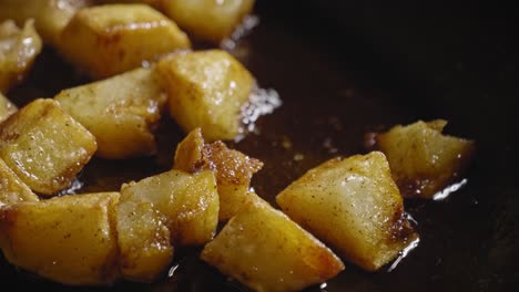Close-up-View-Dices-of-Potatoes-Frying-in-a-Pan,-Wooden-Spoon-Stirring-in-Pan
