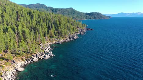 Lake-Tahoe,-California-Lush-Pine-Tree-Forest-And-Crystal-Clear-Turquoise-Waters-With-Mountains-and-Rocky-Shoreline---aerial-drone-pullback