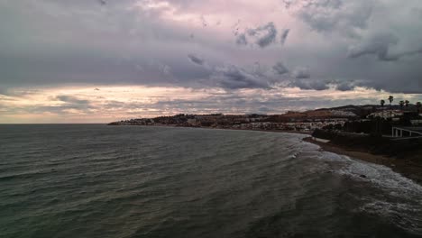 Aerial-coastline-view-of-Mijas,-south-of-Spain,-on-a-dark-cloudy-day-and-moving-backwards