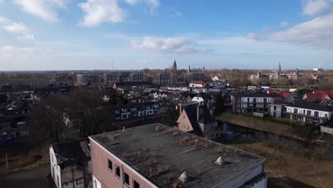 Approach-of-former-youth-prison-facility,-now-abandoned-waiting-for-demolition-and-refurbishment-of-the-moated-plot-field-revealing-wider-cityscape-of-Zutphen-residential-neighbourhoods-and-city