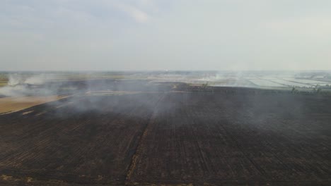 A-reverse-aerial-footage-revealing-a-vast-portion-of-a-farm-land-already-tilled-charred-after-burning,-Grassland-Burning,-Pak-Pli,-Nakhon-Nayok,-Thailand